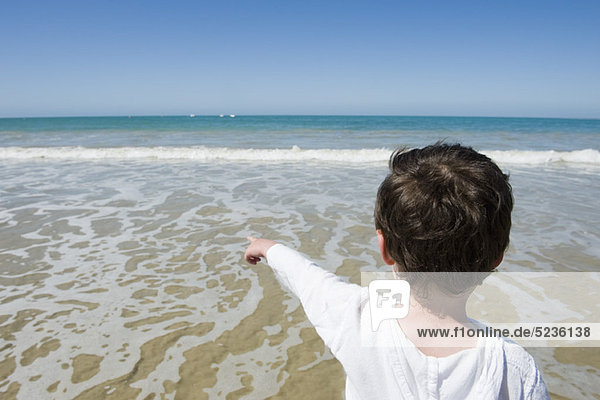 Kleiner Junge am Strand  zeigt auf das Meer  Rückansicht