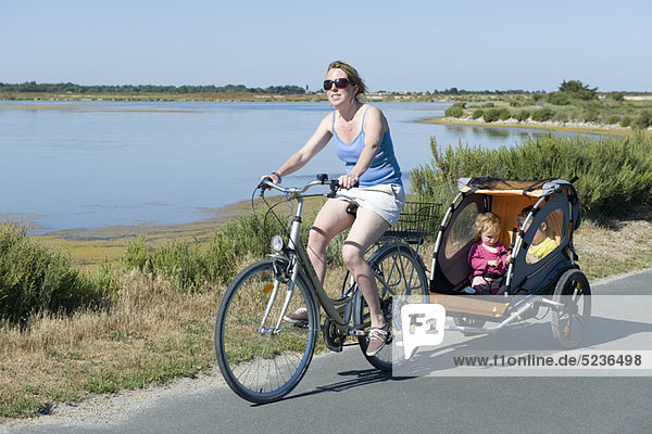 Frau auf dem Fahrradweg mit Kindern im Fahrradanhänger