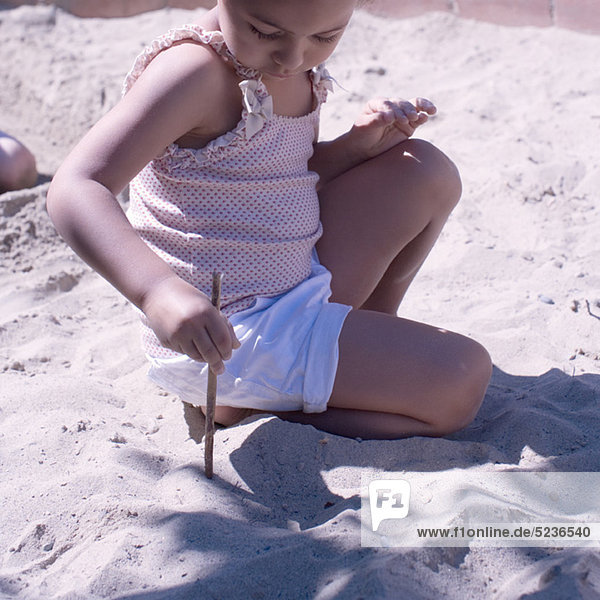 Kleines Mädchen spielt im Sand mit Stock