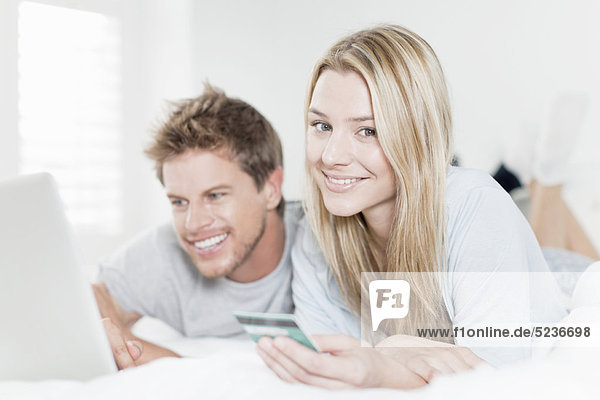Lächelndes Paar beim Online-Shopping im Bett