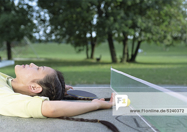 Frau liegt entspannt auf Tischtennis-Tisch im Park