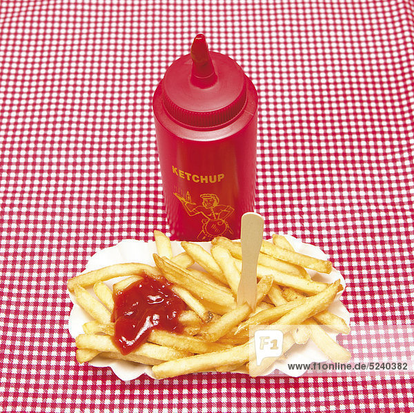 Pommes in Pappschale und Ketchupflasche auf rot-weißer Tischdecke