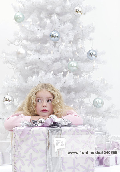 Kleines Mädchen mit großem Paket vor Weihnachtsbaum  nachdenklich