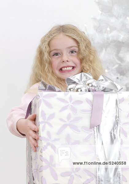 Kleines Mädchen mit schwerem Paket vor Weihnachtsbaum