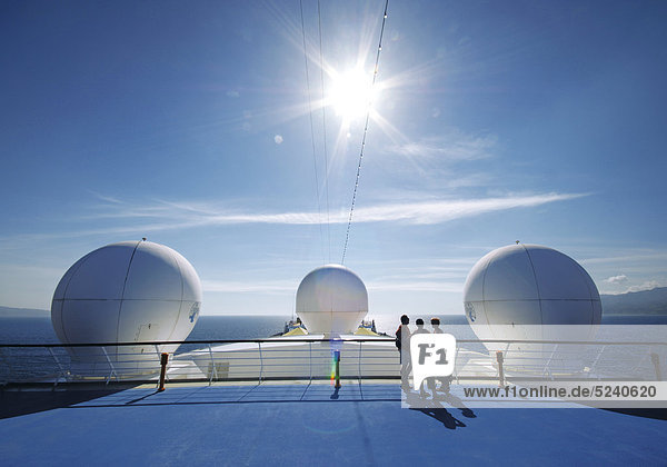 Drei Personen stehen auf Schiffsdeck vor Radar- und Funkanlagen