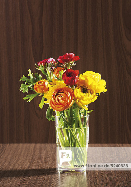 Kleiner  bunter Blumenstrauß in Glas vor Holzhintergrund