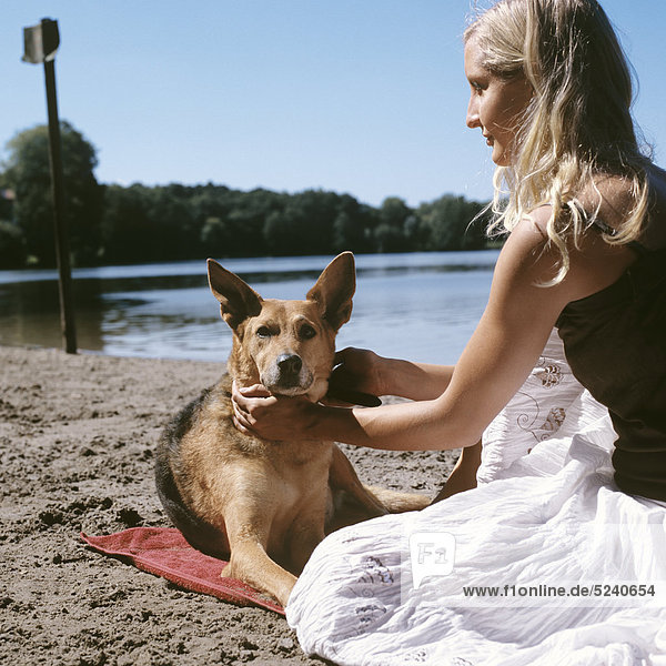 Frau sitzt mit Hund an Seeufer