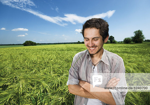 Mann steht mit verschränkten Armen in Getreidefeld  freut sich