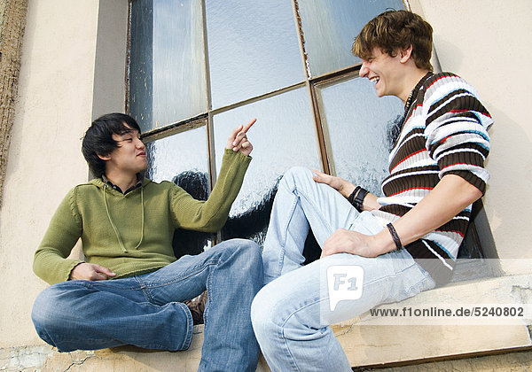Zwei junge Männer  einer asiatisch  sitzen aussen auf Fenstersims