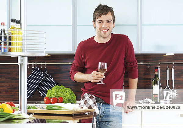 Junger Mann steht mit Weinglas in Küche