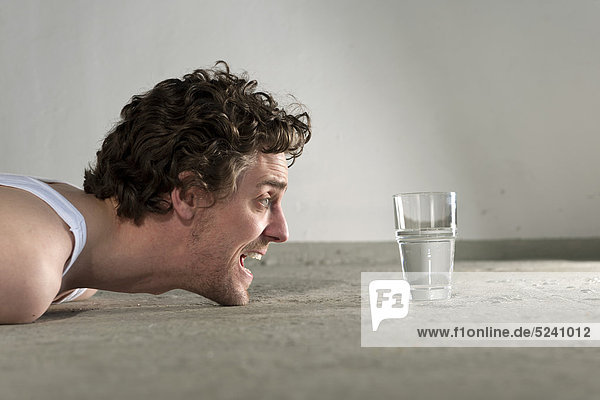 Ein erwachsener Mann  der auf dem Boden liegt und auf ein Glas Wasser starrt.