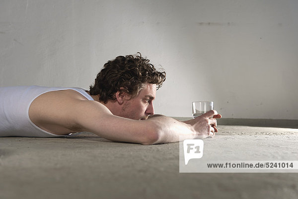 Ein erwachsener Mann  der auf dem Boden liegt und auf ein Glas Wasser starrt.
