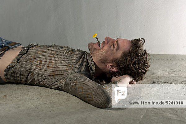 Mittlerer erwachsener Mann  der auf dem Boden liegt und die Blume im Mund hält.
