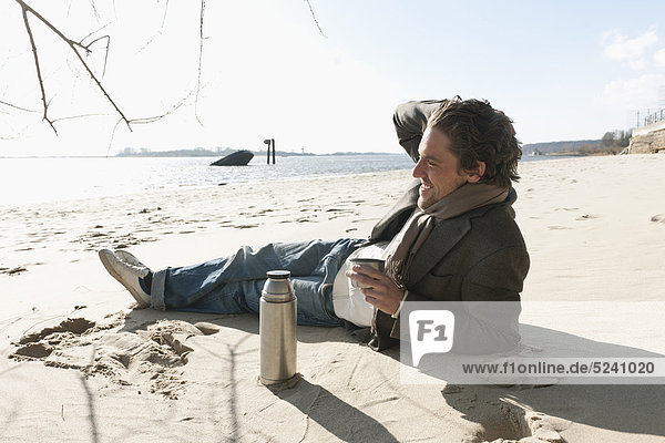 Auf Sand liegender Mann mit Kaffeekanne an der Elbe