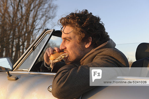 Mann isst Fischsandwich im klassischen Cabrio-Auto