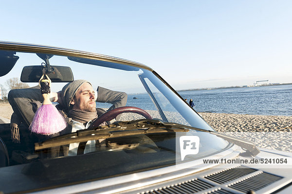 Mann im klassischen Cabriolet an der Elbe sitzend