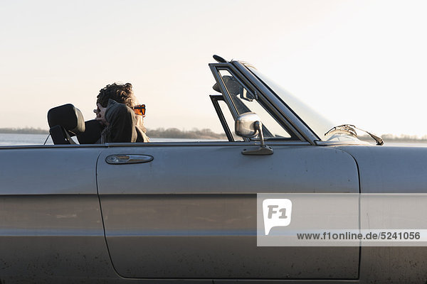 Mann im klassischen Cabriolet an der Elbe sitzend