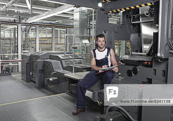 Arbeiter sitzt in Druckerei an Maschine