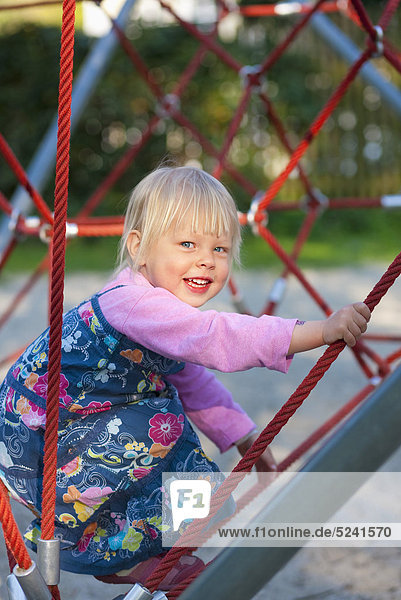Girl climbing on climbing frame in playground  smiling  portrait