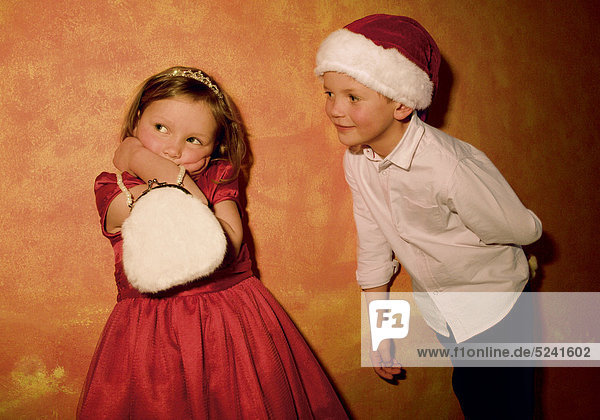 Junge mit Nikolausmütze und Mädchen mit rotem Kleid und weißem Täschchen