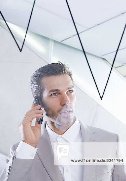 Mann telefoniert im Büro vor Bilanzkurve mit Handy