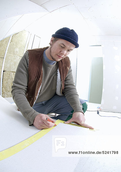 Handwerker auf Baustelle  beim Ausmessen von Rigips-Platten