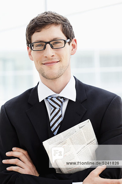 Germany  Bavaria  Diessen am Ammersee  Businesssman standing holding newspaper with folded arms  smiling  portrait