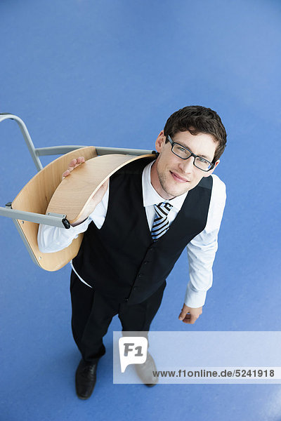 Businessman carrying chair on blue background  smiling  portrait