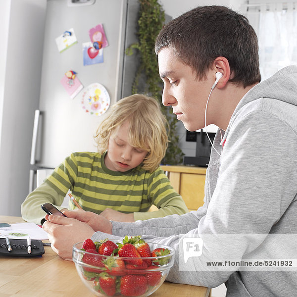 Kleiner Junge und Jugendlicher sitzen zu Hause in Küche