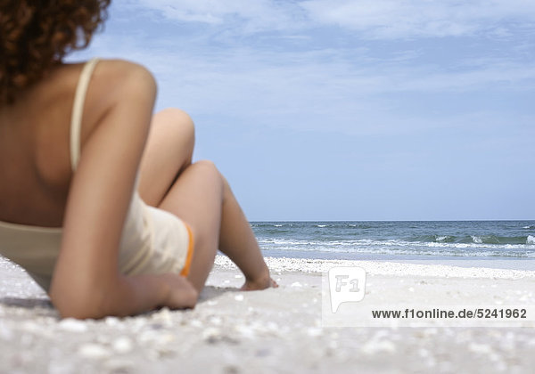 Frau liegt in Bikinihose und Shirt am Strand