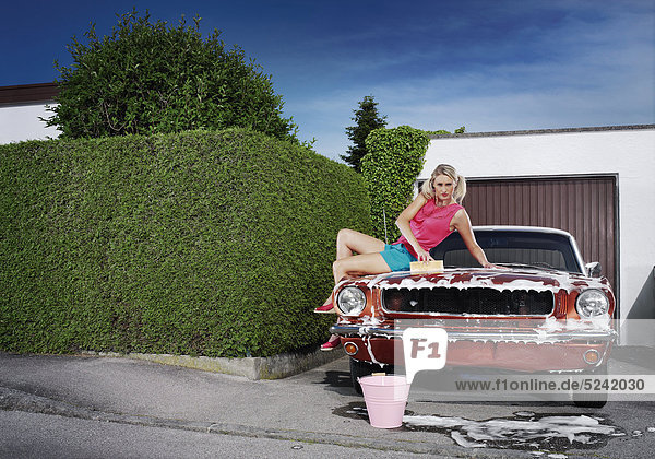 Frau wäscht Oldtimer-Auto  sitzt dabei auf Motorhaube