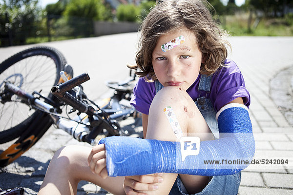 Wounded girl sitting on road after bicycle accident