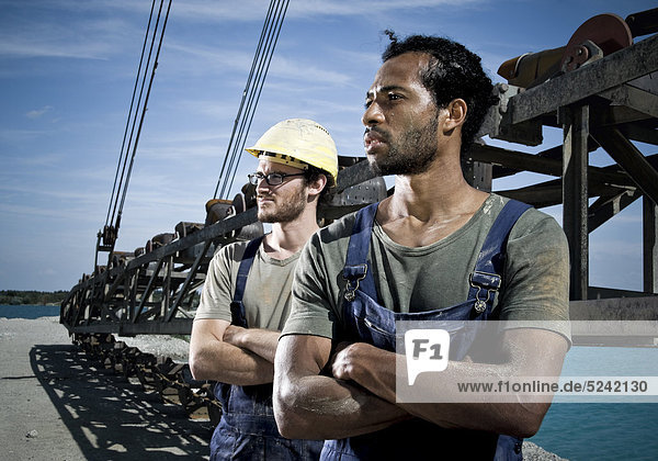 Zwei Arbeiter stehen in Kieswerk vor Stahlkonstruktion  Förderband