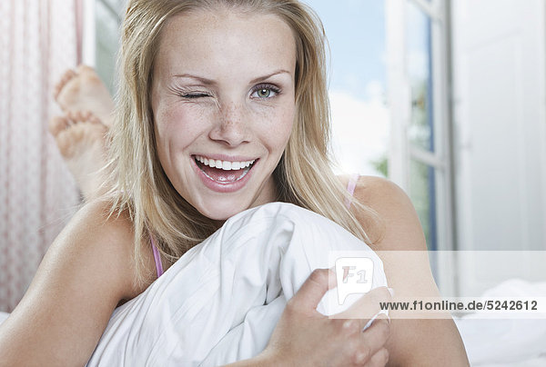 Italy  Tuscany  Young woman lying on bed in hotel room  portrait  winking