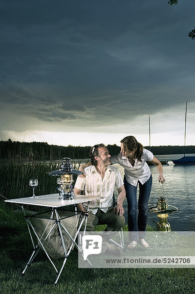 Deutschland  Bayern  Wörthsee  Paar mit Lantrern am Seeufer beim Zelten in der Abenddämmerung