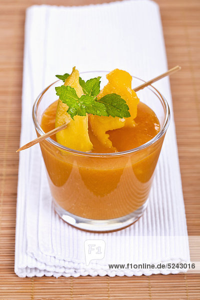 Nahaufnahme von Mango-Smoothie mit Minze und Mangoscheibe auf Cocktail-Stick