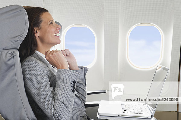 Mittlere erwachsene Geschäftsfrau mit Laptop in der Business Class Flugzeugkabine