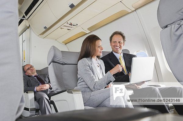 Geschäftsmann und Geschäftsfrau bei der Arbeit am Laptop in der Business Class Flugzeugkabine