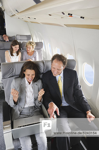 Deutschland  Bayern  München  Geschäftsleute am Laptop in der Business Class Flugzeugkabine  lächelnd