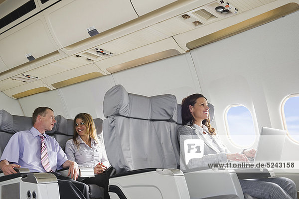 Deutschland  Bayern  München  Geschäftsleute im Gespräch und mit Laptop in der Business Class Flugzeugkabine  lächelnd