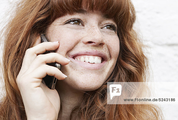 Nahaufnahme einer jungen Frau  die am Handy spricht und lächelt.