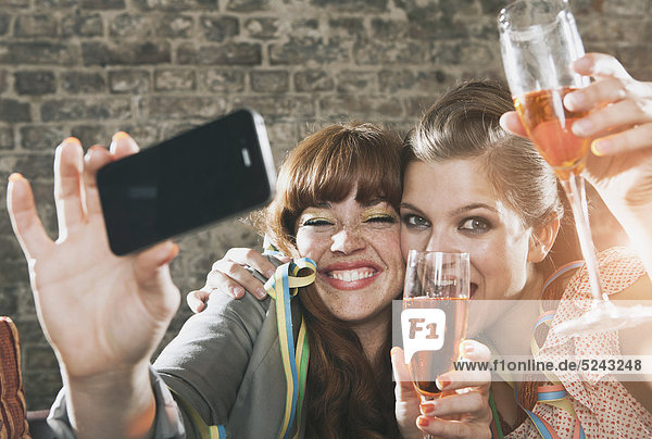 Close up of young women holding champagne glass and photographing with cell phone  smiling