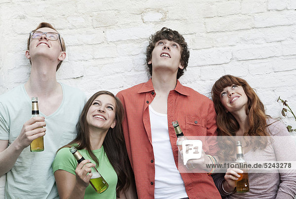 Junge Männer und Frauen  die Bierflaschen halten und lächelnd aufblicken.