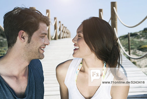 Spanien  Mallorca  Junges Paar auf Strandpromenade sitzend  lächelnd