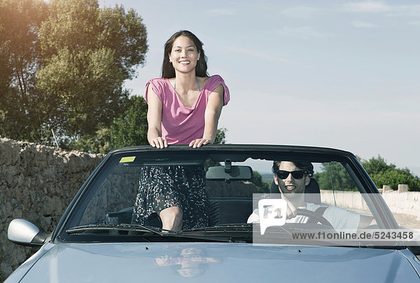 Spanien  Mallorca  Junger Mann fährt und Frau steht im Cabriolet