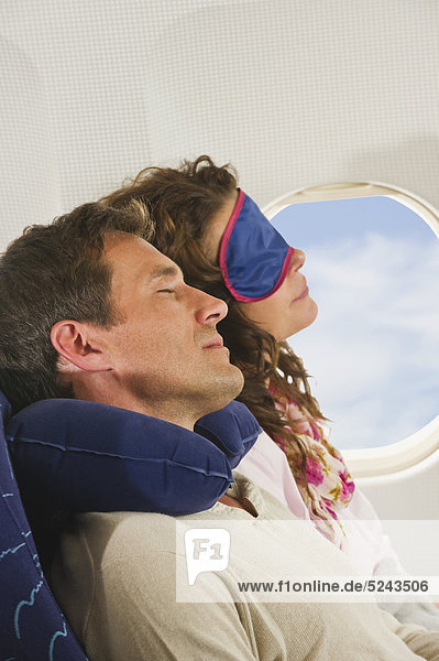 Germany  Munich  Bavaria  Mid adult couple wearing sleep mask and sleeping in economy class airliner
