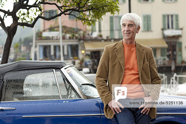 Senior lehnt an Oldtimer am Hafen  Italien  Linfano