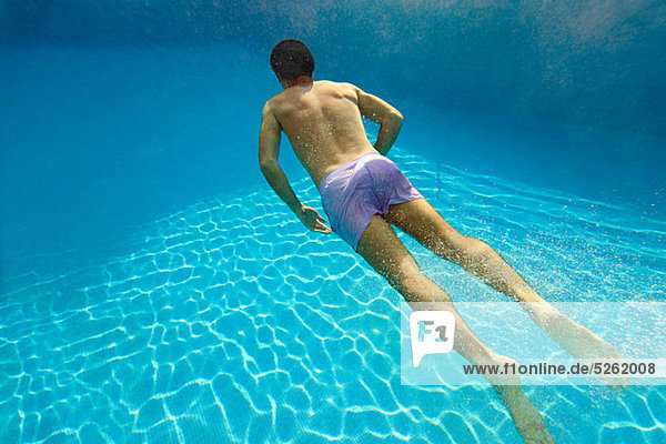 Young man swimming underwater in swimming pool