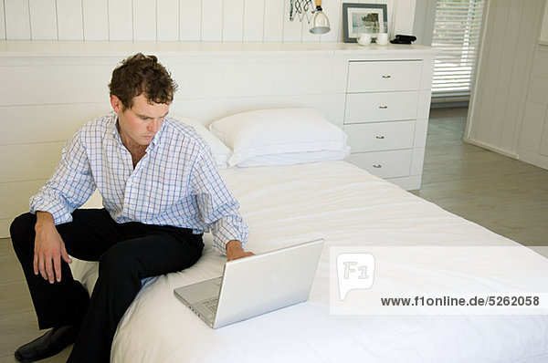Man sitting on bed using laptop