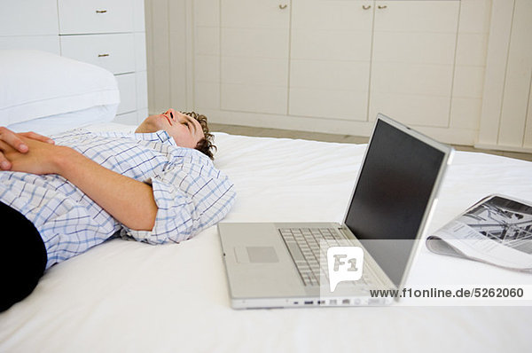 Mann liegt auf dem Bett mit Laptop